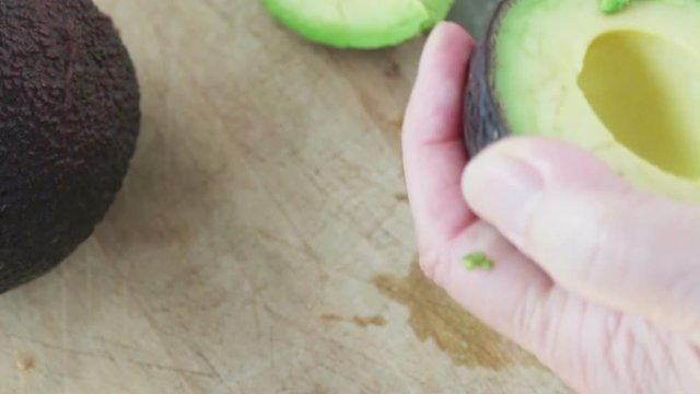 A woman removes avocado half with a spoon, and cuts it into slices