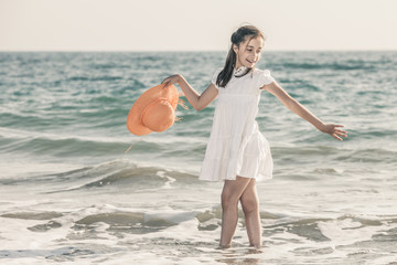 girl on the seashore wearing an orange hat and a white dress