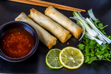 Oriental, Plate with spring rolls chop sticks, three spring rolls, spring onions, lime, lemon, sweet chilli sauce.