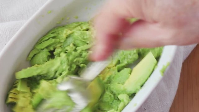 A woman mashes an avocado and adds lemon juice
