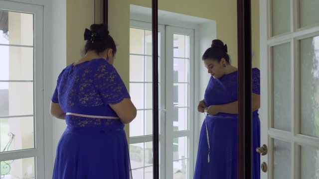 Fat girl in a blue dress in front of a mirror