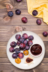 Appetizing bruschetta from fresh bread with plum jam and ripe berries of blue plums on a plate on a wooden table. Top view