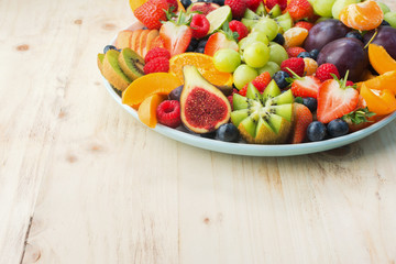 Healthy fruit and berries platter, strawberries raspberries oranges plums apples kiwis grapes blueberries on the light wooden pine table, close up, copy space for text, square, selective focus