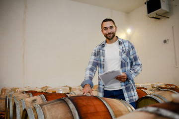 Fototapeta premium handsome man winemaker in a maturing wine cellar winery during harvest season with oak barrels