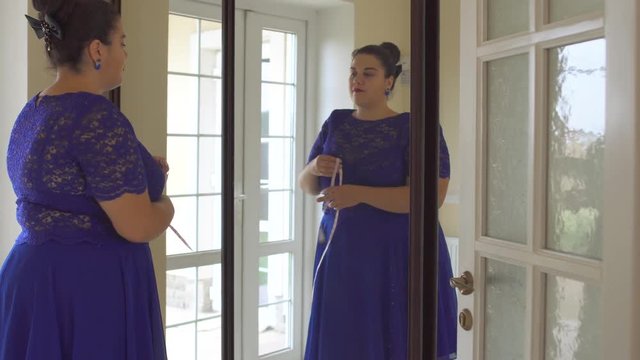 Fat girl in a blue dress in front of a mirror