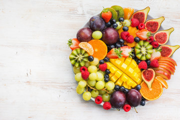 Healthy raw fruits and berries plate, strawberries raspberries oranges plums apples kiwis grapes blueberries, mango, figs on the white woorden table, top view, copy space, selective focus