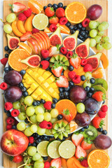 Healthy raw fruits and berries platter background, strawberries raspberries oranges plums apples kiwis grapes blueberries, mango on the serving board, top view, vertcial