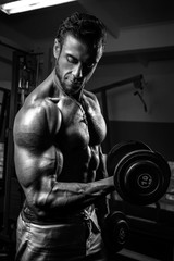 Fototapeta na wymiar White Muscular man training his biceps in the gym by dumbbells BW