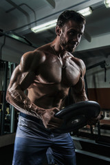 Fototapeta na wymiar White Muscular man is posing in the gym with weight plate and straining muscles
