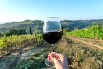 Wine glass over beautiful landscape of Tuscany, with green valley of grapes and hills around. Wine beverage tasting in Italy during harvest