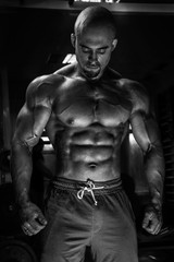 Fototapeta na wymiar White Muscular man fitness model is posing in the gym and looking down BW