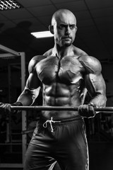 Fototapeta na wymiar White Muscular man training his arms in the gym by barbell BW
