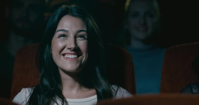 An attractive young woman smiling and laughing in a movie theatre. Slow motion tracking shot.
