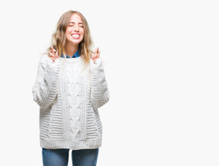 Beautiful young blonde woman wearing winter sweater over isolated background smiling crossing fingers with hope and eyes closed. Luck and superstitious concept.