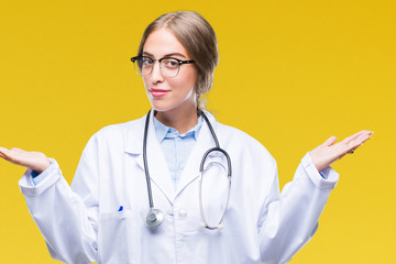 Beautiful young blonde doctor woman wearing medical uniform over isolated background clueless and confused expression with arms and hands raised. Doubt concept.
