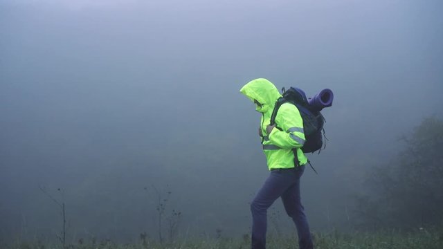 Man tourist in signal vest in hood with backpack walking in fog alone,close up