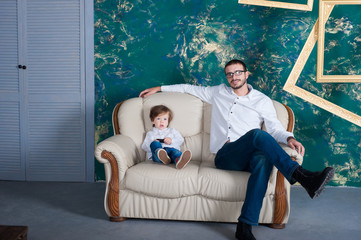 happy man and his arms embrace his son. Family mod on the sofa at home. White shirt. Father's Day