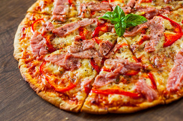 slices of Pizza with Mozzarella cheese, ham, pepper, meat, Tomatoes, Spices and Fresh Basil. Italian pizza on wooden background