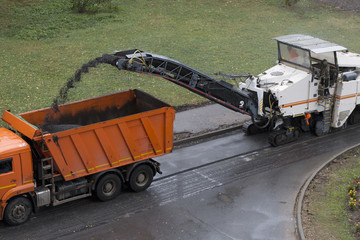 Road milling machine removes old asphalt and loads milled asphalt into the dump truck. Road repair process