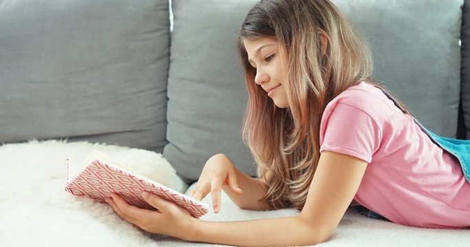Portrait teenage girl reading book, lying on the sofa indoors