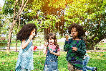 Obraz premium Happy children in a field trips and playing blowing bubbles together in the green park, Outside school education concept