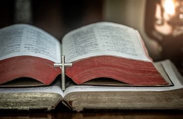Obraz premium Close up the cross on the Bible opening beside the oil lamp on wooden table.