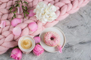 Cup with cappuccino, doughnut, pink pastel giant blanket, flowers, bedroom, morning concept