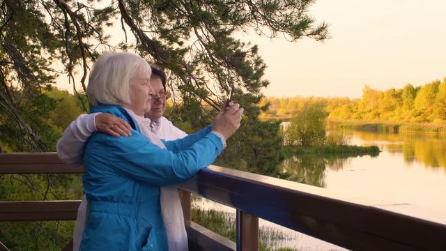 Two elderly woman making selfie photo to smart phone on autumn landscape
