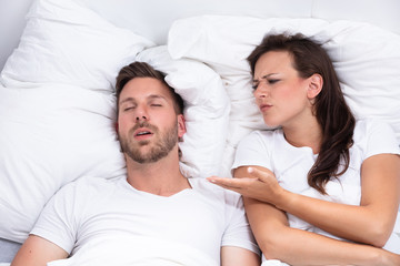 Woman Covering Her Ears While Man Snoring On Bed