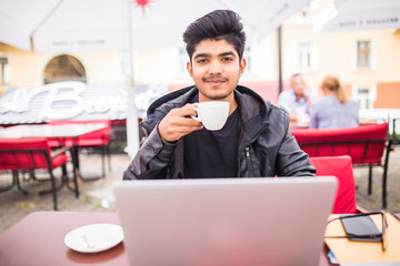 Young indian guy drinking coffee while computing at a student cafe