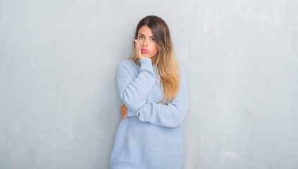 Young adult woman over grey grunge wall wearing winter outfit thinking looking tired and bored with depression problems with crossed arms.