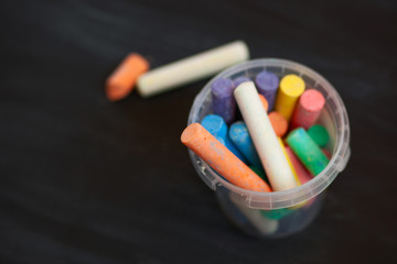 Color chalk in plastic cans closeup on blackboard. Selective focus