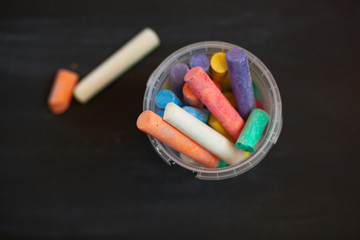 Color chalk in plastic cans closeup on blackboard. Selective focus