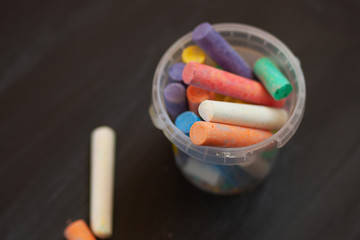 Color chalk in plastic cans closeup on blackboard. Selective focus