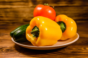 Ceramic plate with cucumbers, tomatoes and sweet pepper on wooden table