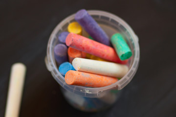 Color chalk in plastic cans closeup on blackboard. Selective focus