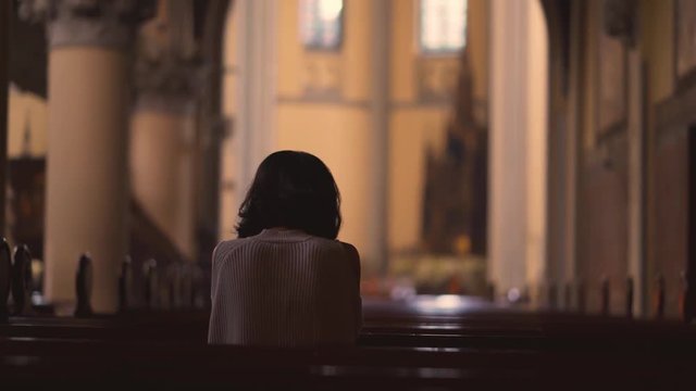 Rear view of a young Christian woman praying to GOD while sitting in the church. Shot in 4k resolution
