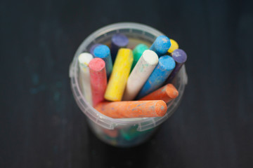 Color chalk in plastic cans closeup on blackboard. Selective focus