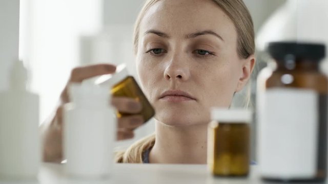 Close up shot of young Caucasian woman looking into medicine cabinet, taking bottle of pills and going away