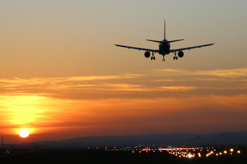 Naklejka na ściany i meble Plane landing at runway on the background of sunset