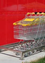 Stack of new shiny shopping carts in a supermarket with red wall in background