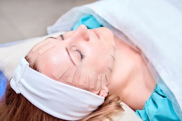 Obraz na płótnie Canvas Taping. Caucasian woman lying with tape on her face. Physiotherapy and cosmetology procedure. Method of non-surgical skin rejuvenation. Facial skin treatment