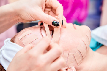 Kinesiotaping. Beautician sticking tape on the face of a woman. Physiotherapy and cosmetology procedure. Method of non-surgical skin rejuvenation. Facial skincare