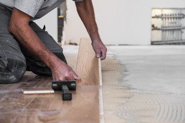 Worker installing wooden flooring boards on applied adhesive