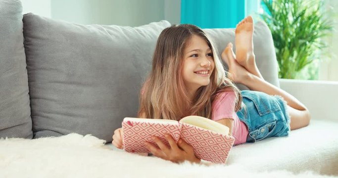 School girl holding her notebook, smiling, lying on the sofa