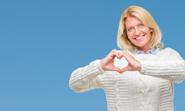 Middle age blonde woman wearing winter sweater over isolated background smiling in love showing heart symbol and shape with hands. Romantic concept.