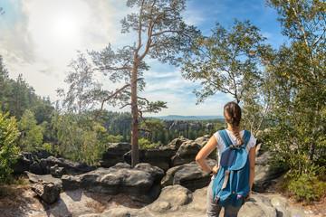 Junge Frau mit Zopf und blauem Rucksack im Elbsandsteingebirge mit Aussicht auf die Schrammsteine