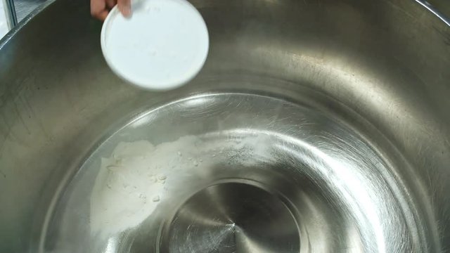 Hands of unrecognizable cook adding flour into empty industrial dough kneading machine at factory