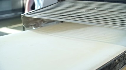 Close up shot of laminated dough for croissants being rolled in dough sheeter machine at factory - Powered by Adobe