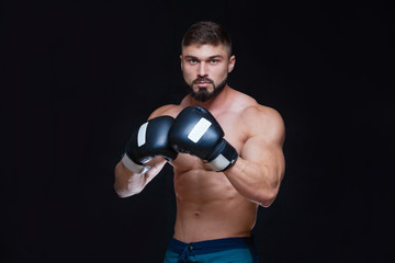Strong muscular boxer in black boxing gloves. Isolated on black background.